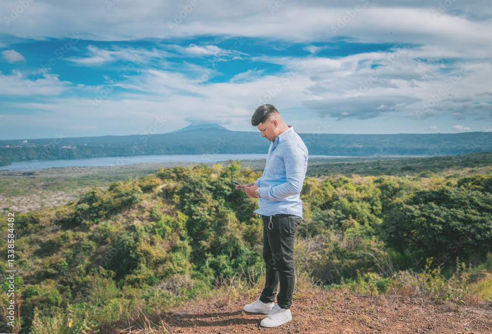 Young man using phone at a viewpoint surrounded by nature. Person using his phone at a beautiful scenic viewpoint, Masaya Young man using phone at a viewpoint surrounded by nature. Person using his phone at a beautiful scenic viewpoint, Masaya
