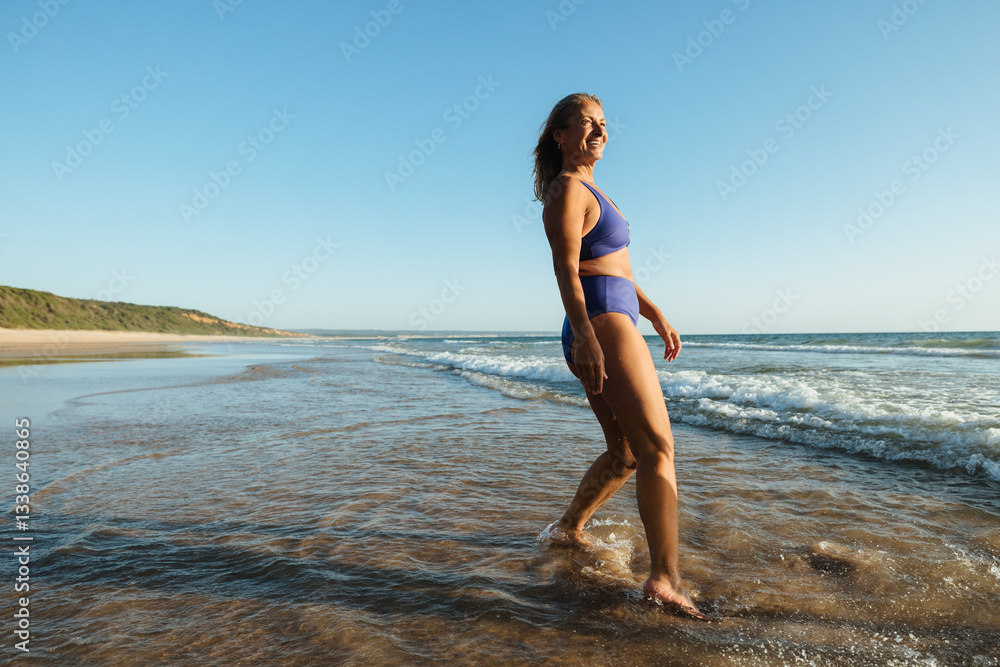 Fototapeta premium Mature woman enjoying a carefree day walking on the sandy beach