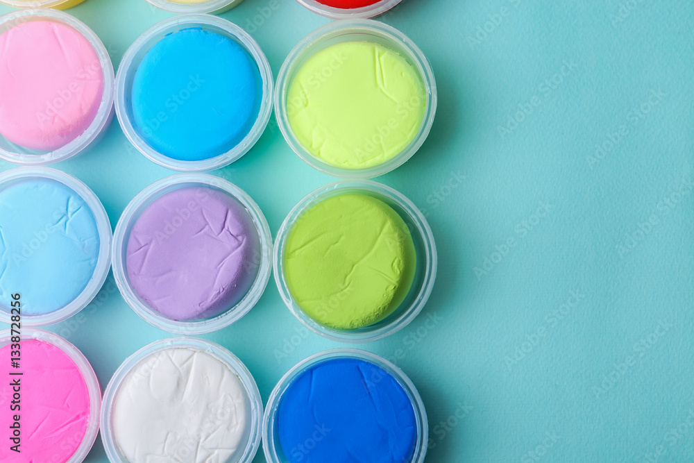 Different colorful modeling clay in plastic jars on light blue background, flat lay. Space for text Different colorful modeling clay in plastic jars on light blue background, flat lay. Space for text