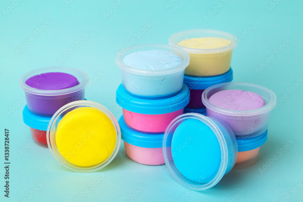 Different colorful modeling clay in plastic jars on light blue background Different colorful modeling clay in plastic jars on light blue background