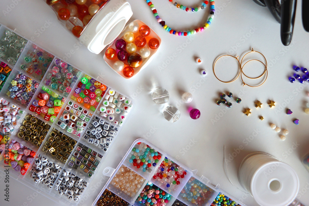 Hand figurine, colorful friendship bracelets, necklaces, various beads and DIY supplies on the table. Making jewelry at home. Flat lay.