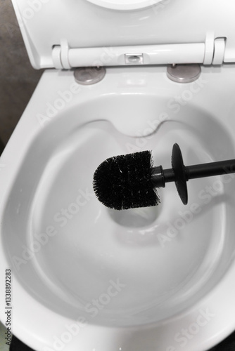 Black toilet brush hovering above an open, pristine white toilet bowl, highlighting the importance of bathroom hygiene and promoting a sense of cleanliness and freshness