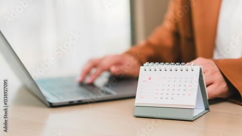 Obraz na płótnie Monthly calendar April 2025 on desk beside professional using laptop, illustrating schedule planning, daily tasks organization, productivity management, and business deadlines. w salonie