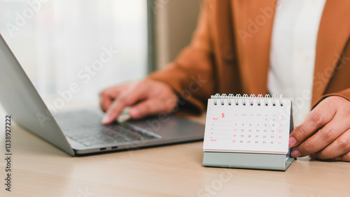 Obraz na płótnie Monthly calendar May 2025 placed on office desk next to professional working with laptop, illustrating business schedule, daily planning, task management, deadlines, and productivity enhancement. w salonie