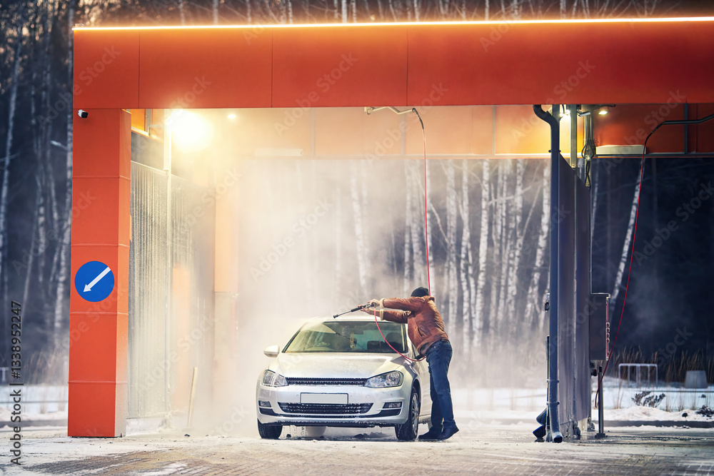 Man using high-pressure spray nozzle at self-service car wash to clean car, removing dirt and grime with water spray at an outdoor contactless washing station. Contactless car cleaning technology
