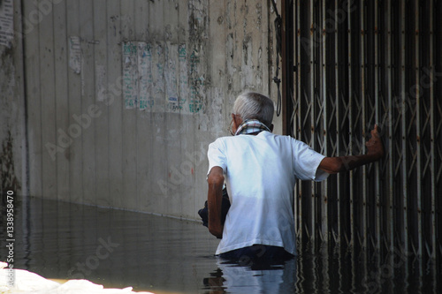 Thai old men people natural disaster victims walking wading in water on street while water flood and inundation road wait help rescue and donations at countryside rural city in Nonthaburi, Thailand