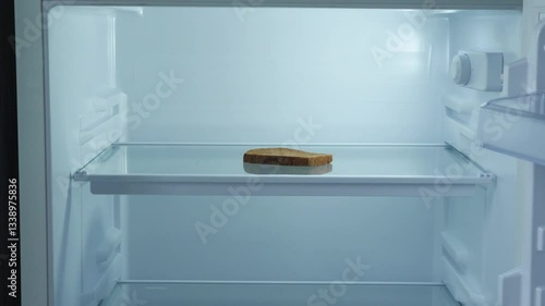 a piece of bread in an empty refrigerator is taken by a man's hand, the concept of food shortage, food crisis