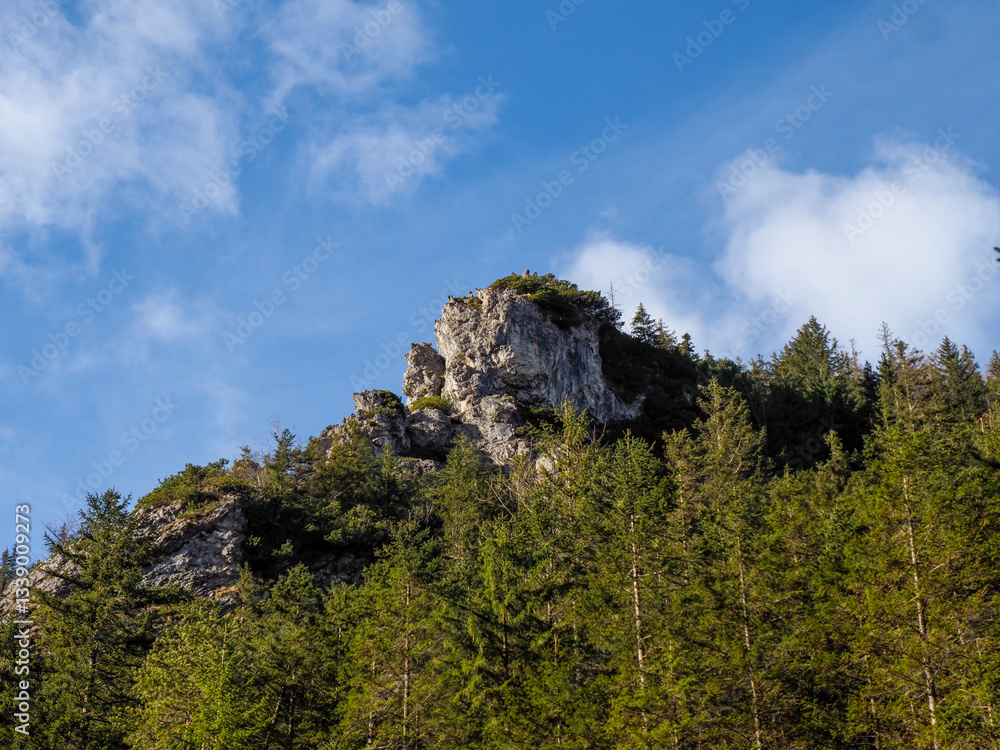 Towering Limestone Cliff Formation Against Blue Sky with Scattered Clouds and Vibrant Spring Forest Canopy Towering Limestone Cliff Formation Against Blue Sky with Scattered Clouds and Vibrant Spring Forest Canopy