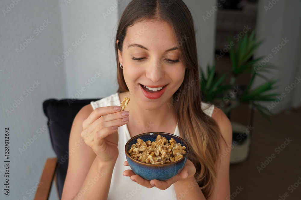 Healthy Brazilian woman eating walnuts from bowl at home Healthy Brazilian woman eating walnuts from bowl at home