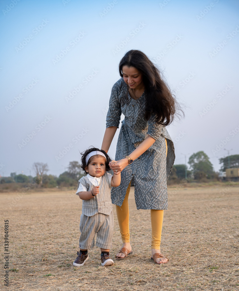 Fototapeta premium First Steps. Adorable smiling Indian mother walks with her infant son 