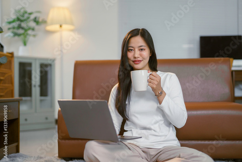 Foto Smiling asian freelancer sipping coffee during remote work on laptop at home wor