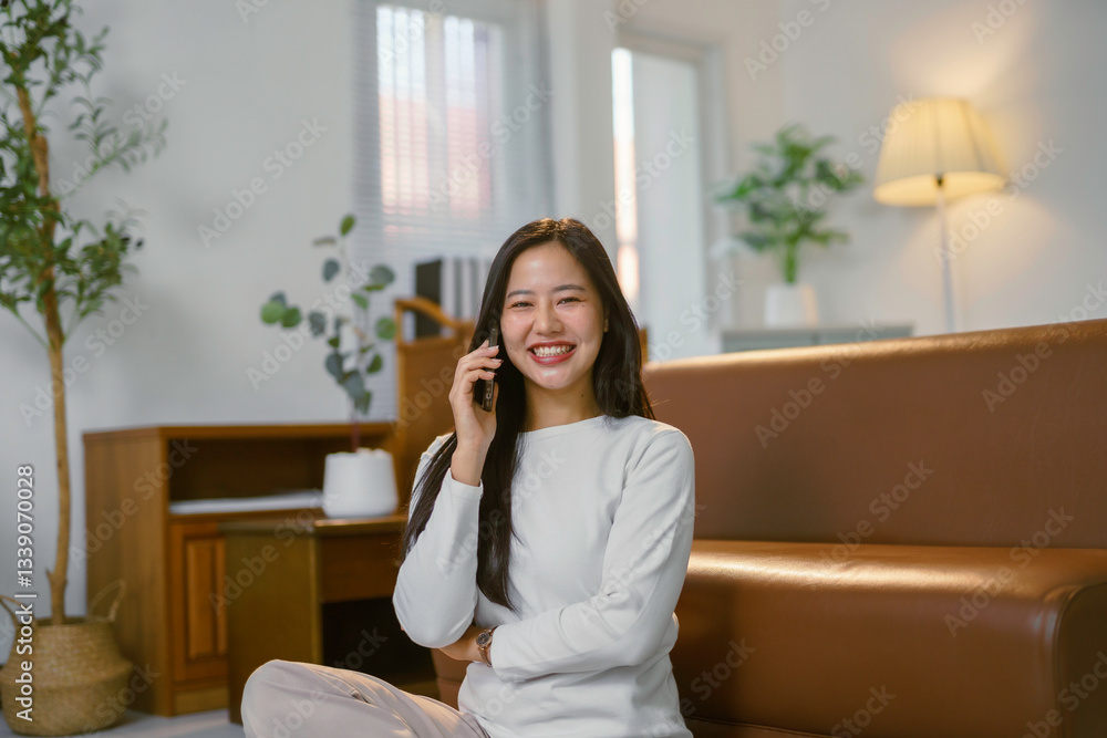 Happy freelancer talking on the phone and smiling while sitting on the floor near sofa at home Happy freelancer talking on the phone and smiling while sitting on the floor near sofa at home