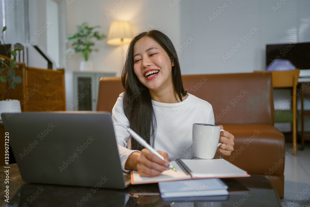 Young Asian woman working from home, drinking coffee and taking notes while laughing during a video call Young Asian woman working from home, drinking coffee and taking notes while laughing during a video call