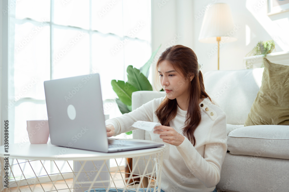 Young Woman Enjoys Organizing Receipts While Using a Laptop in a Cozy Living Room During Daylight Young Woman Enjoys Organizing Receipts While Using a Laptop in a Cozy Living Room During Daylight