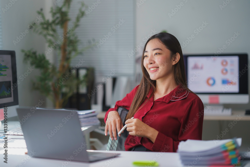 Young happy Asian businesswoman smiling and working with laptop computer in modern office, looking away from the screen Young happy Asian businesswoman smiling and working with laptop computer in modern office, looking away from the screen