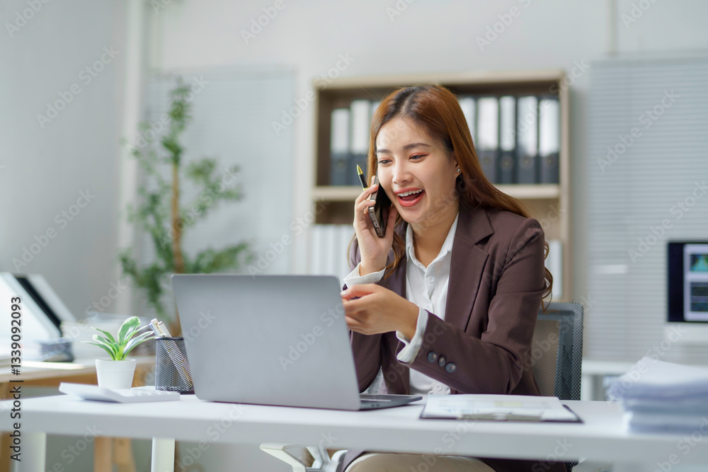 Young happy asian businesswoman talking on mobile phone and working on laptop computer in modern office, business and technology concept Young happy asian businesswoman talking on mobile phone and working on laptop computer in modern office, business and technology concept