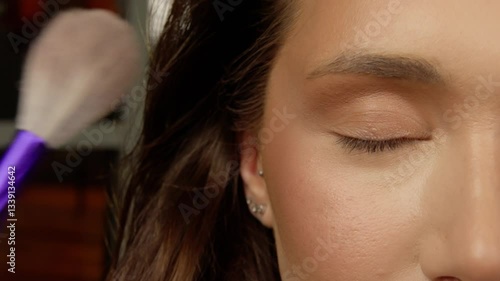 Makeup artist applying shimmering eyeshadow on model's eyelid, using delicate professional brush with meticulous precision during beauty makeover