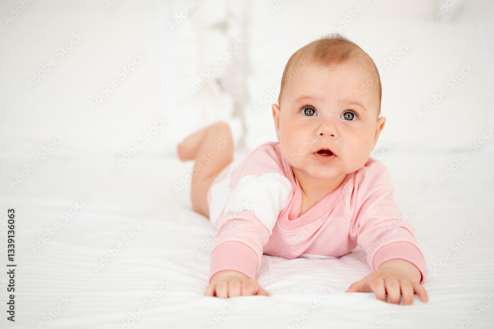 A baby girl smiles or laughs lying on her tummy, a cute and smiling little baby in a pink bodysuit on a white bed at home. A baby girl smiles or laughs lying on her tummy, a cute and smiling little baby in a pink bodysuit on a white bed at home.