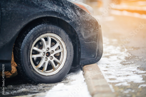 Vehicle parked improperly, front bumper touching the curb in icy conditions, risks of winter driving, slippery roads, and potential collision hazards. Car front bumper dangerously positioned on curb