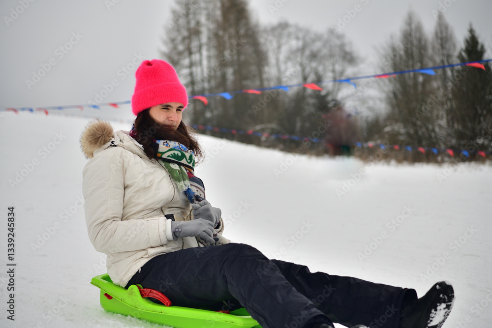 Girl sledding downhill on snow in winter and laughing with joy