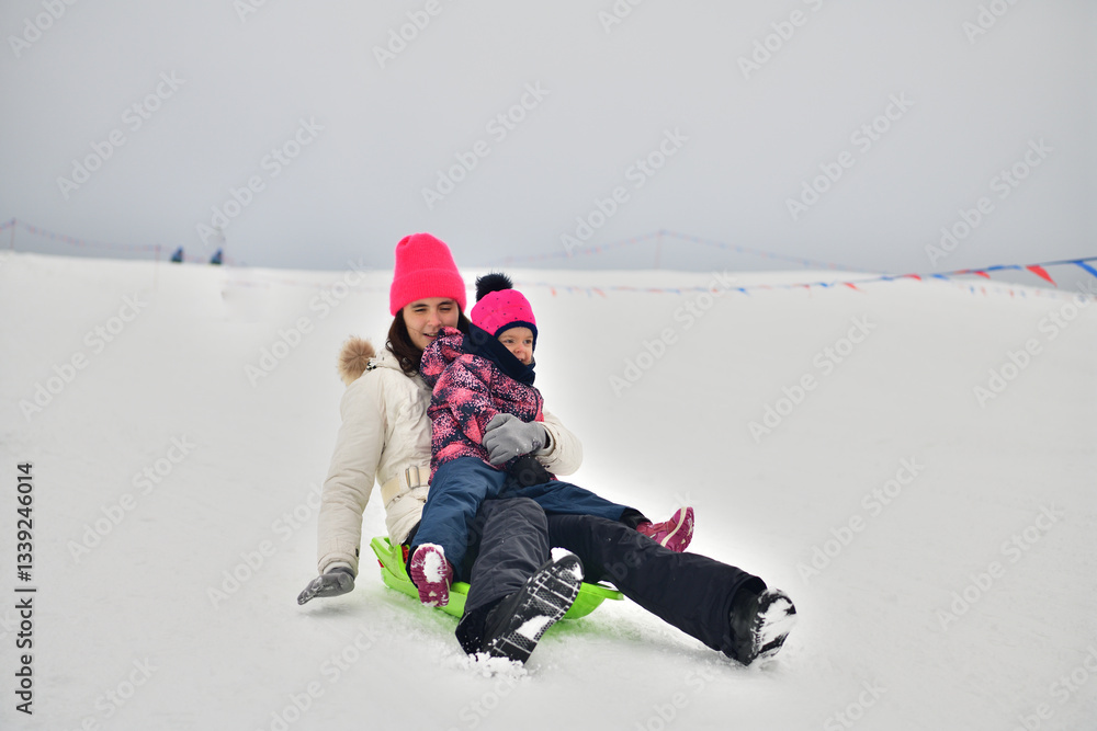 Two girls are tobogganing downhill on snowy hill in winter