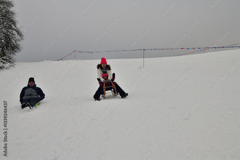 Family tobogganing down a snowy hill during winter vacation