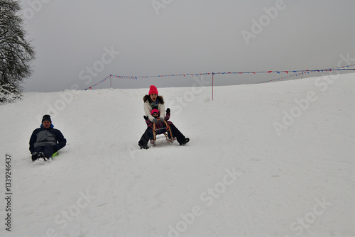 Family tobogganing down a snowy hill during winter vacation