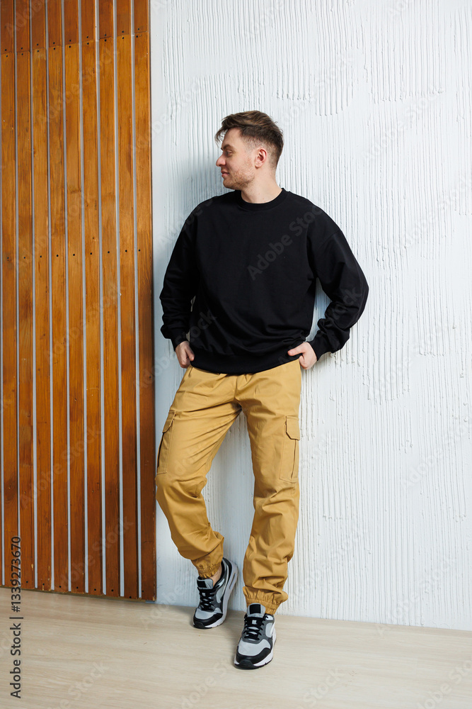A man in a black sweatshirt and yellow pants leans on a wall