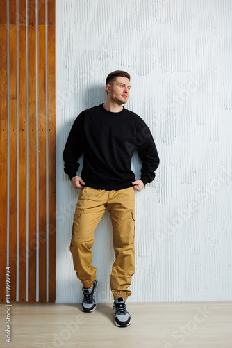 Obraz na płótnie A man in a black sweatshirt and yellow pants leans against a wall w salonie