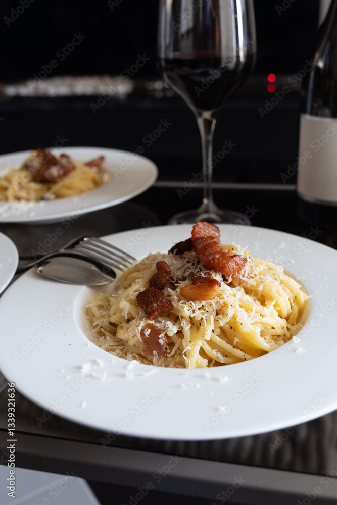 Fototapeta premium Close up of plate of closeup carbonara spaghetti topped with grilled bacon with red wine in background.