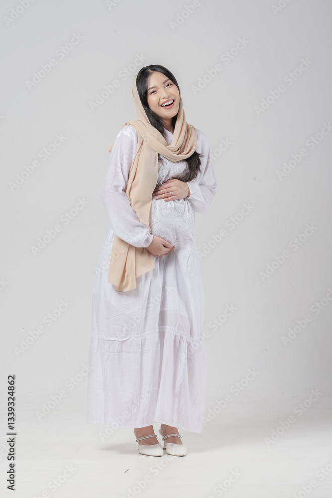 Happy Asian Muslim pregnant woman wearing veil hijab smiling while touching her stomach. Happy Asian Muslim pregnant woman wearing veil hijab smiling while touching her stomach.