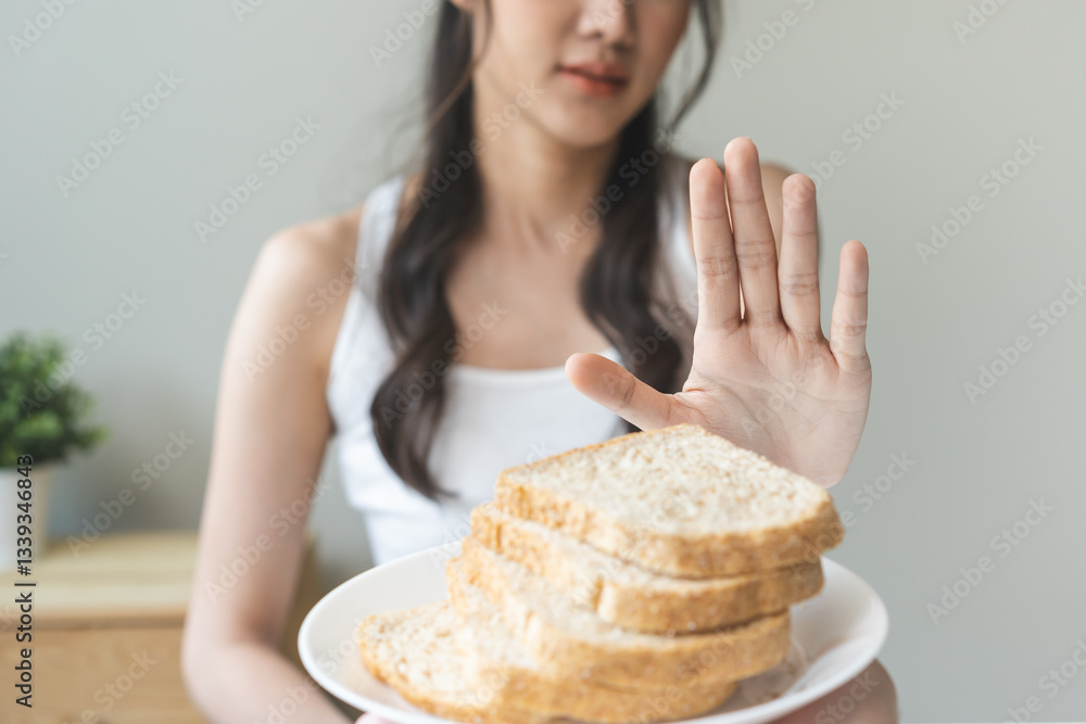 Gluten allergy, asian young woman hand push out, refusing to eat white bread slice on plate in breakfast food meal at home, girl having a stomach ache. Gluten intolerant and Gluten free diet concept.