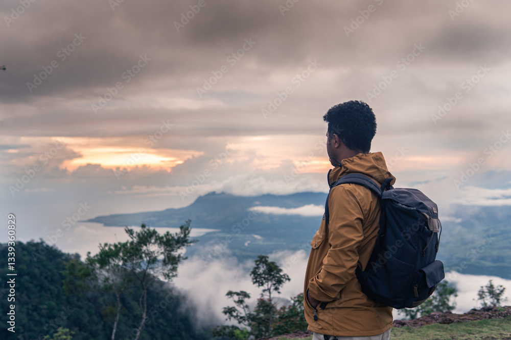 A traveler stands on a mountain peak at sunrise, gazing at the misty valley and ocean. Wearing a backpack and jacket, he embraces adventure, freedom, and exploration in a peaceful natural setting. A traveler stands on a mountain peak at sunrise, gazing at the misty valley and ocean. Wearing a backpack and jacket, he embraces adventure, freedom, and exploration in a peaceful natural setting.