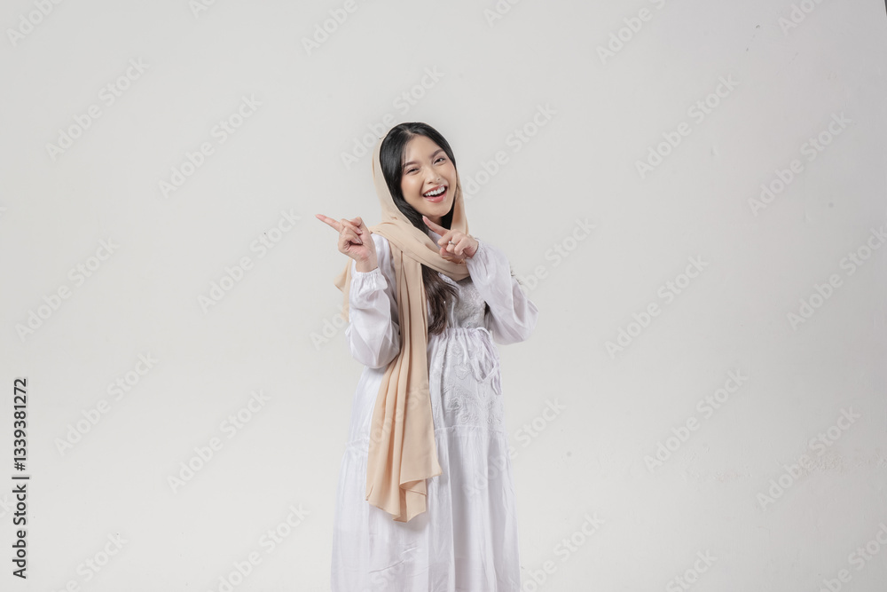 Beautiful Asian Muslim pregnant woman in hijab pointing to the copy space behind her. Beautiful Asian Muslim pregnant woman in hijab pointing to the copy space behind her.
