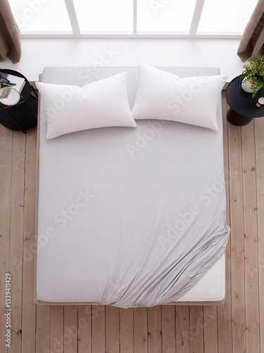 Double bed with two white pillows, covered with a gray fitted sheet with an elastic band and two black bedside tables. The corner of the mattress is visible. Top view photo. Suitable for mockups.