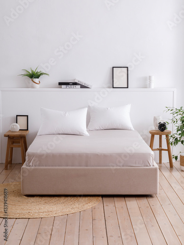 Modern bedroom with white walls, wooden floors and handcrafted furniture. Double bed with two pillows neatly covered with a grey fitted sheet. Front view photo. Suitable for mockup