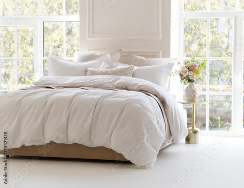 Sunny bedroom with two large windows. Four pillows, cushion and a fluffy down comforter on a double bed with bedside table and bouquet in vase on it. Side view horizontal photo. Suitable for mockup
