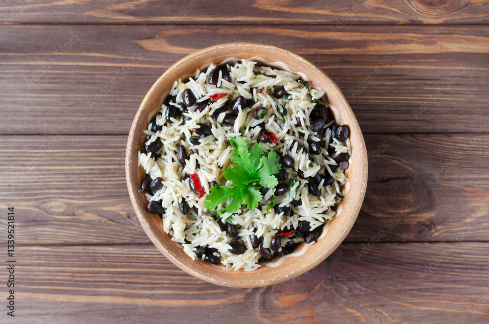 Traditional Costa Rican dish - Gallopinto. Black beans and rice stewed with onions, garlic, cilantro in a ceramic bowl on a wooden table. Selective focus. Horizontal orientation. Top view . Copy space Traditional Costa Rican dish - Gallopinto. Black beans and rice stewed with onions, garlic, cilantro in a ceramic bowl on a wooden table. Selective focus. Horizontal orientation. Top view . Copy space