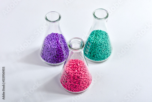 Red, purple and turquoise masterbatch granules in Erlenmeyer flask isolated on white background, color pigment carrier polymer in plastic industry. Perfect for plastic company catalog design