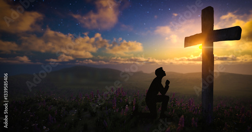 Silhouette of a man praying in front of the cross on a meadow with moving clouds