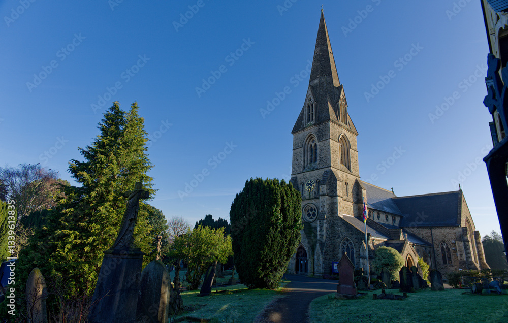 Beautiful old Christ Church in Swindon, UK. Wide view of the church with graveyard and green trees. Footpath towards the entrance on a sunny morning with blue sky.