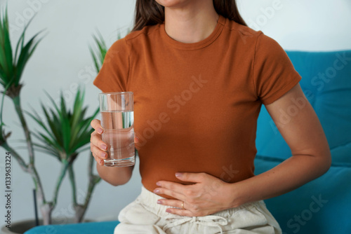 Eating Disorder. Unrecognizable girl suffering from abdominal pain holds a glass of water in her hand. Unregulated Intestine.