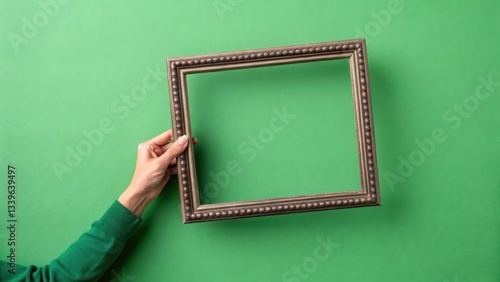Hand holding picture frame with green screen on a plain green background