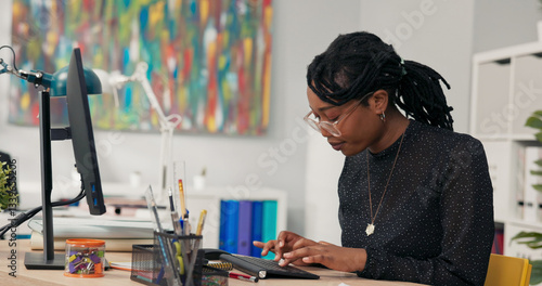 Attractive, experienced, dark-skinned company secretary sits in office in front of a computer tapping fingers on keyboard writing e-mails, filling out documents, reports, preparing minutes for manager