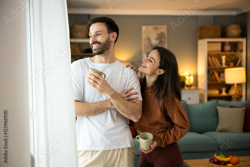 A smiling couple shares a joyful moment with coffee mugs, showcasing their connection in a cozy indoor setting.