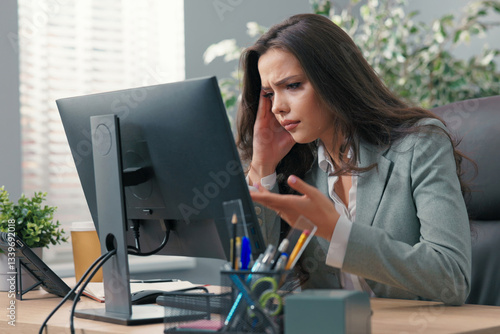 Beautiful busy businesswoman sits at desk in front of computer in office, has technical problems with monitor, wrong screen setting, no signal, error, keyboard not working