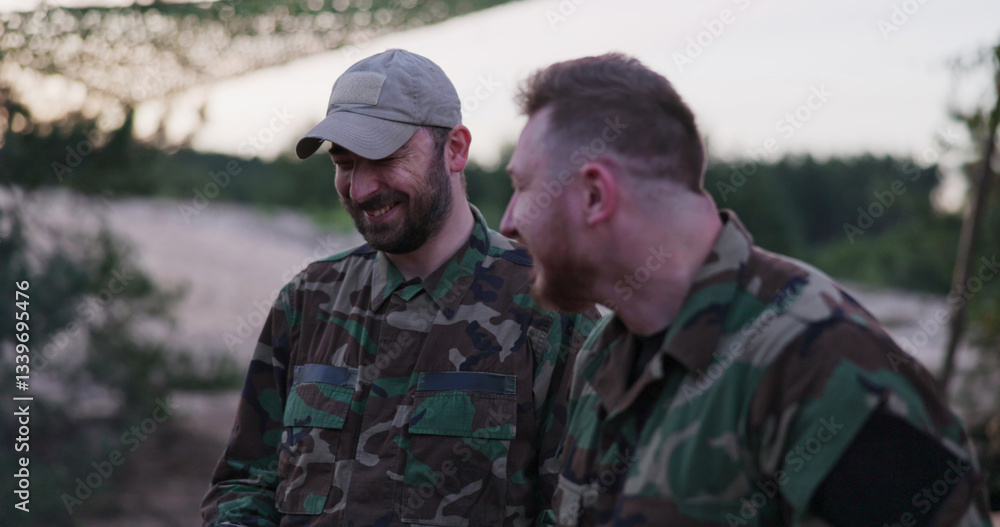 Fototapeta premium Soldiers in camouflage clothing gather around a campfire in the evening, frying sausages for supper, joking, laughing, and relaxing after a long day of service and field exercises.