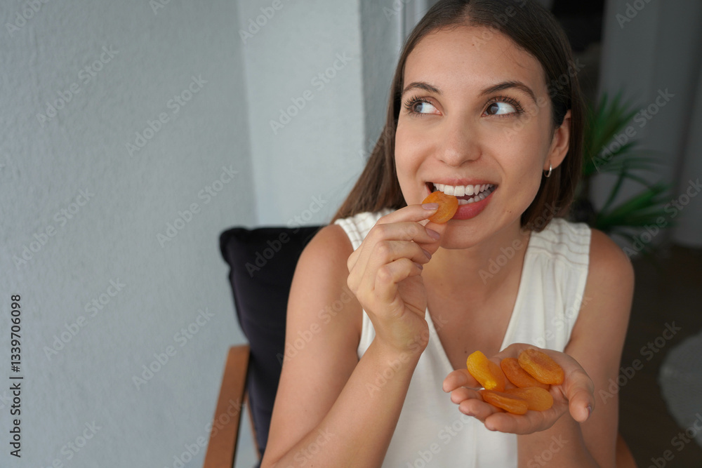 Hispanic girl biting apricots dried at home. Looks to the side.