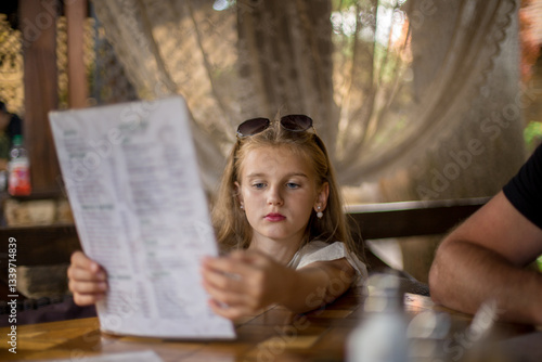A girl with long white hair reads the menu in a restaurant. The girl has earrings and sunglasses on her head.