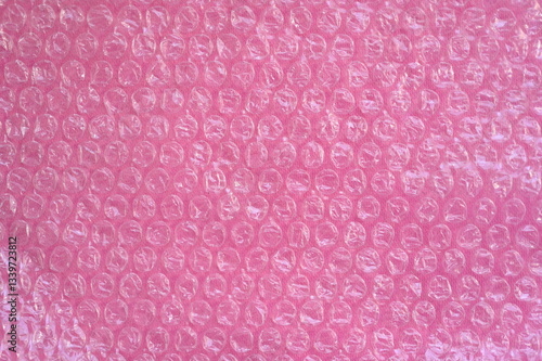 Close-up of the texture of pink bubble wrap as a background. Transparent air-filled pockets create a structured, homogeneous pattern with a shiny, reflective surface. The bright pink colour accentua
